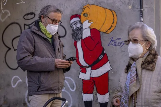 A man and woman wearing FFP2 masks to curb the spread of COVID-19 are seen in front of a mural depicting Santa Claus, in Madrid, Spain, Wednesday, January 12, 2022. Italy, Spain and other European countries are re-instating or stiffening mask mandates as their hospitals struggle with mounting numbers of COVID-19 patients. (Photo by Manu Fernandez/AP Photo)