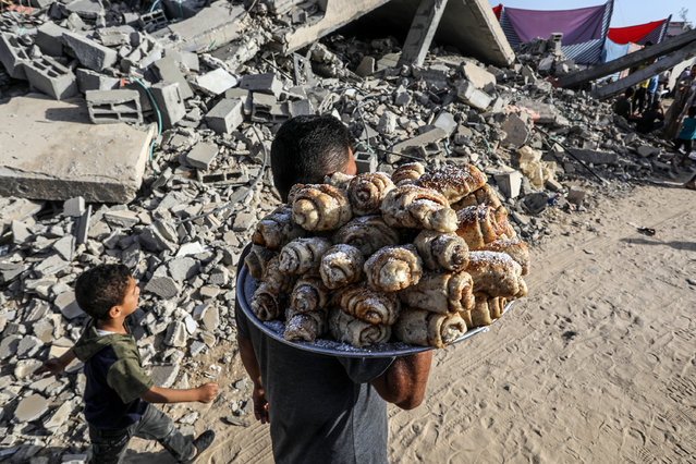 A Palestinian man distributes sweet buns within Eid al-Adha among the rubble of buildings destroyed by Israeli attacks in Khan Yunis, Gaza on June 16, 2024. (Photo by Abed Rahim Khatib/Anadolu via Getty Images)