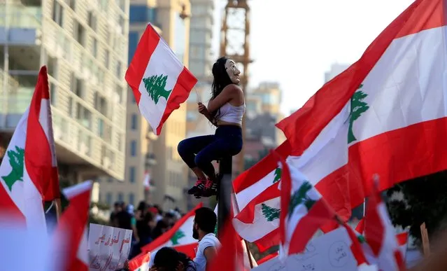 A demonstrator sits on a pole while carrying a national flag during an anti-government protest in downtown Beirut, Lebanon on October 20, 2019. (Photo by Ali Hashisho/Reuters)