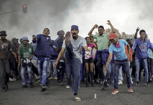 Protesters sing and chant in front of a burning barricade in the Ennerdale, Johannesburg township, Tuesday May 9, 2017. Violent protests have erupted in South Africa's biggest city for a second day, with police firing rubber bullets at demonstrators who blocked roads and burned tires. (Photo by AP Photo)