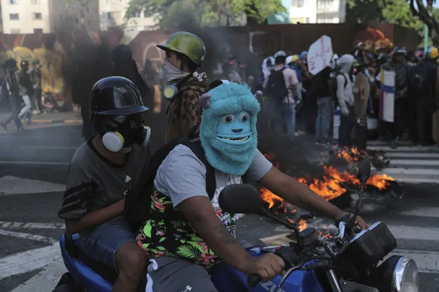An anti-government protester wearing a mask depicting the Monster Inc. character Sulley drives a motorbike through a barricade set up by fellow protesters, in Caracas, Venezuela, Thursday, May 18, 2017. (Photo by Fernando Llano/AP Photo)