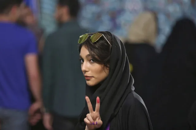 A voter flashes a victory sign with her inked finger while voting for the presidential and municipal councils election at a polling station in Tehran, Iran, Friday, May 19, 2017. Millions of Iranians voted late into the night Friday to decide whether incumbent President Hassan Rouhani deserves another four years in office after securing a landmark nuclear deal, or if the sluggish economy demands a new hard-line leader who could return the country to a more confrontational path with the West. (Photo by Vahid Salemi/AP Photo)