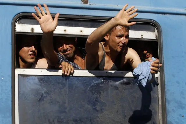 In this photo taken on Thursday, July 23, 2015 migrants wave from a window of a train departing to Serbia at the railway station in the southern Macedonian town of Gevgelija. (Photo by Boris Grdanoski/AP Photo)