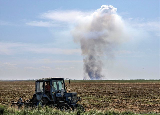 An agricultural worker operates a tractor as smoke rises in the distance after a military strike, amid Russia's attack on Ukraine, in Kherson region, Ukraine on June 20, 2023. (Photo by Andrii Dubchak/Reuters)