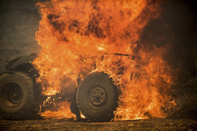Flames from a wildfire consume an all-terrain vehicle near Oroville, Calif., on Saturday, July 8, 2017. Residents were ordered to evacuate from several roads in the rural area as flames climbed tall trees. The California Department of Forestry and Fire Protection reported that several residents and one firefighter suffered minor injuries. (Photo by Noah Berger/AP Photo)
