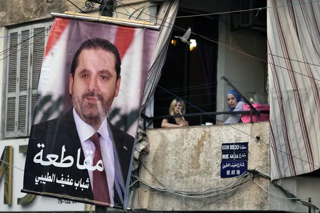 Women sit on their apartment balcony and smoke a water pipe next to of a poster of former Lebanese Prime Minister Saad Hariri with Arabic reading “Boycott (the elections)”, in Beirut, Lebanon, Tuesday, May 10, 2022. Given Lebanon's devastating economic meltdown, Sunday's parliament election (May 15) is seen as an opportunity to punish the current crop of politicians that have driven the country to the ground. (Photo by Bilal Hussein/AP Photo)