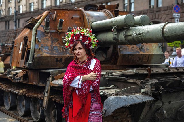 A woman dressed in Ukrainian national costume poses for a photograph in front destroyed Russian military equipment at Khreshchatyk street in Kyiv on August 20, 2022, that has been turned into an open-air military museum ahead of Ukraine's Independence Day on August 24, amid Russia's invasion of Ukraine. (Photo by Dimitar Dilkoff/AFP Photo)