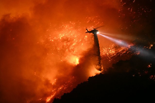 A fire fighting helicopter drops water as the Palisades fire grows near the Mandeville Canyon neighborhood and Encino, California, on January 11, 2025. The Palisades Fire, the largest of the Los Angeles fires, spread toward previously untouched neighborhoods January 11, forcing new evacuations and dimming hopes that the disaster was coming under control. Across the city, at least 11 people have died as multiple fires have ripped through residential areas since January 7, razing thousands of homes in destruction that US President Joe Biden likened to a “war scene”. (Photo by Patrick T. Fallon/AFP Photo)
