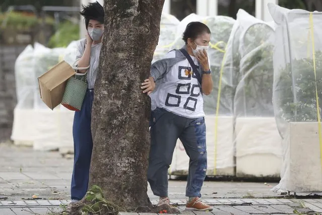 Pedestrians hold a tree to protect themselves from strong winds as Typhoon Hinnamnor hits in Naha, Okinawa prefecture, Japan Sunday, September 4, 2022. (Photo by Kyodo News via AP Photo)