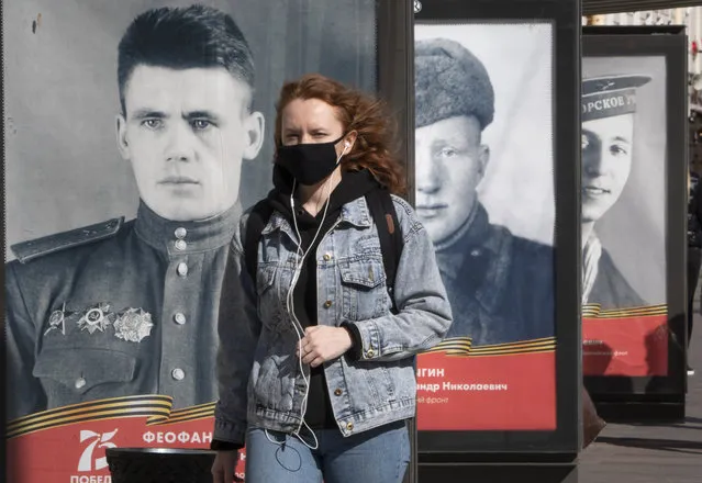 A woman wearing a face mask to protect against coronavirus walks past posters with portraits of the Soviet Army soldiers, participants in World War II during celebration of the 75th anniversary of the defeat of the Nazis in World War II in St.Petersburg, Russia, Saturday, May 9, 2020. Victory Day, the anniversary of the defeat of Nazi Germany in World War II, is Russia's most important secular holiday and this year's observance had been expected to be especially large because it is the 75th anniversary, but military parades in Russian cities and a mass processions called The Immortal Regiment were postponed as part of measures to stifle the spread of coronavirus. (Photo by Dmitri Lovetsky/AP Photo)