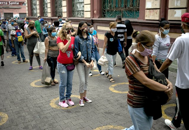 People stand over yellow circles painted on pavement that serve as visual cues to help shoppers adhere to social distancing as a precaution against the spread of the new coronavirus, before entering a popular market in the neighborhood of Catia in Caracas, Venezuela, Thursday, May 28, 2019. (Photo by Ariana Cubillos/AP Photo)