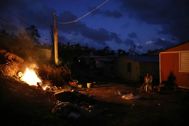A resident sits outside her home, which lacks electricity, as a trash fire burns on December 21, 2017 in San Isidro, Puerto Rico. The community was hard-hit by Hurricane Maria and remains mostly without grid electricity. Barely three months after Hurricane Maria made landfall, approximately one-third of the devastated island is still without electricity. While the official death toll from the massive storm remains at 64, The New York Times recently reported the actual toll for the storm and its aftermath likely stands at more than 1,000. Puerto Rico's governor has ordered a recount as the holiday season approaches. (Photo by Mario Tama/Getty Images)