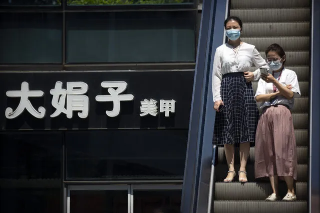 People wearing face masks to protect against the coronavirus ride an escalator past a sign of a nail salon at a shopping and office complex in Beijing, Tuesday, August 11, 2020. Mainland China and semi-autonomous Hong Kong saw declines in their recent outbreaks Tuesday. (Photo by Mark Schiefelbein/AP Photo)