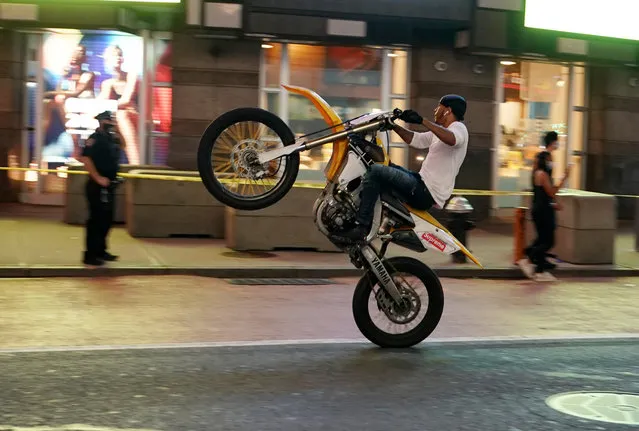 A man pops a wheelie on a dirt bike on W 42nd Street in front of an NYPD officer during the summer of the coronavirus pandemic in New York, NY on August 13, 2020. (Photo by Christopher Sadowski/The New York Post)