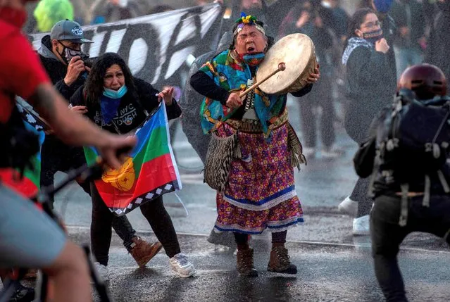 A Mapuche indigenous woman plays a drum as a riot police use water cannons to disperse demonstrators during a protest against the government's handling of the COVID-19 novel coronavirus pandemic, in Santiago, on September 4, 2020. Anti-government protests return to Chile as lockdown measures against the pandemic ease. (Photo by Martin Bernetti/AFP Photo)