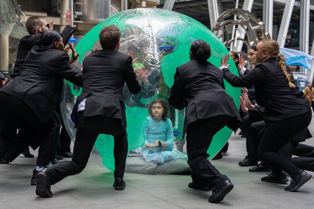 A young girl (name not given) sits in an inflatable Earth as dancers working with Mothers Rise Up (a group of UK mothers protesting about climate change) hold a performance protest outside Lloyds of London on February 26, 2024 in London, United Kingdom. Organised by Mothers Rise Up, a climate activism group advocating for every child's right to a safe climate and clean air, this performance was crafted with Denni Sayers, a mother, choreographer, and director in opera and theatre. (Photo by Carl Court/Getty Images)
