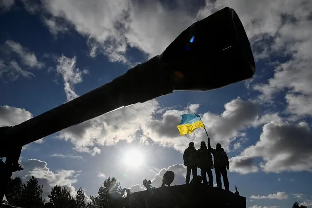Ukrainian personnel hold a Ukrainian flag as they stand on a Challenger 2 tank during training at Bovington Camp, near Wool in southwestern Britain on February 22, 2023. (Photo by Toby Melville/Reuters)