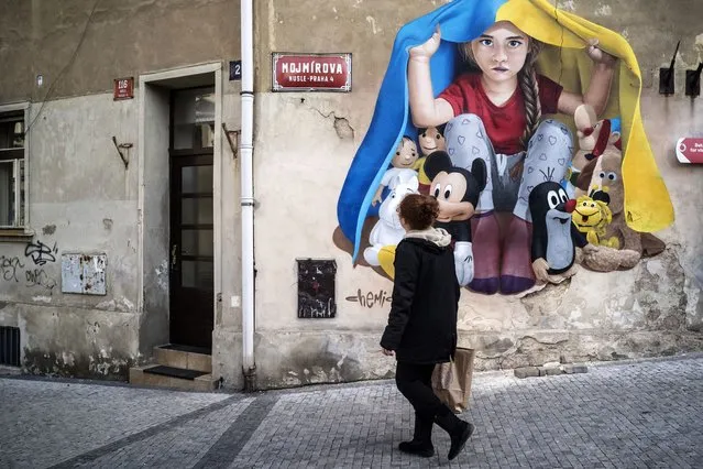 A woman walks past a graffiti mural, showing a child protecting with a Ukrainian flag against the war, made by artist ChemiS, on March 19, 2022 in Prague. (Photo by Michal Cizek/AFP Photo)