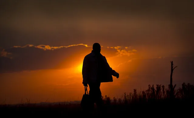 A man walks home at sunset past recently-deployed South African military personnel in the politically-sensitive mining town of Bekkersdal, where there have been recent disputes between supporters of incumbent President Jacob Zuma's African National Congress (ANC) party and supporters of rival Julius Malema's Economic Freedom Fighters (EFF) party, in South Africa Monday, May 5, 2014. (Photo by Ben Curtis/AP Photo)
