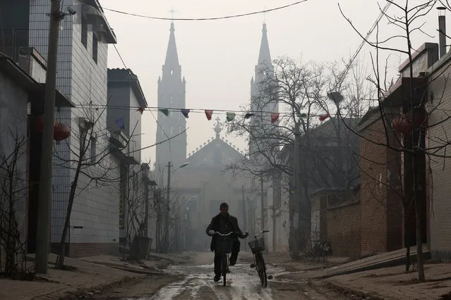 A man cycles down a road in front of the Sacred Heart of Jesus Church in Wuqiu village, Hebei Province, China, December 11, 2016. (Photo by Thomas Peter/Reuters)