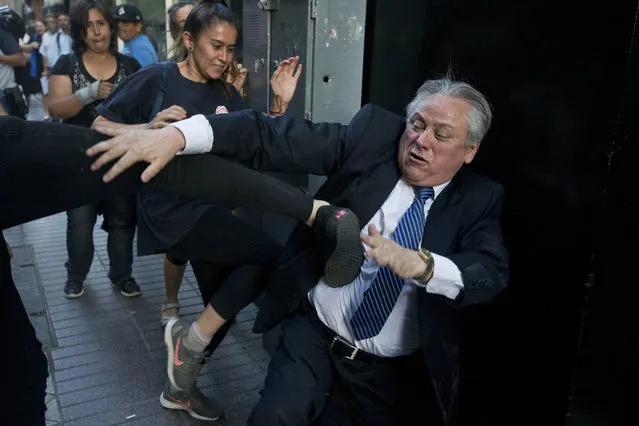 Ivan Arostica, president of Chile's Constitutional Court, ties to avoid a kick by a protester as he leaves the court, which listened to arguments in favor and against conditional freedom for those convicted of human rights crimes, in Santiago, Chile, on Wednesday, December 19, 2018. Protesters fear a ruling in favor could benefit the prisoners of Punta Peuco, a prison for state agents convicted of murder during the 1973-1990 dictatorship of Augustus Pinochet. (Photo by Esteban Felix/AP Photo)