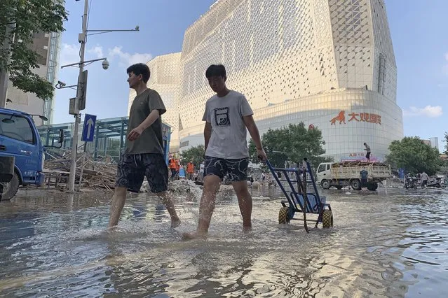 Residents walk along a flooded road in the aftermath of the heaviest recorded rainfall in Zhengzhou in central China's Henan province on Saturday, July 24, 2021. Rescuers used bulldozers and rubber boats to move residents out of flooded neighborhoods in central China on Saturday after torrential rains killed at least 56 people. (Photo by Dake Kang/AP Photo)