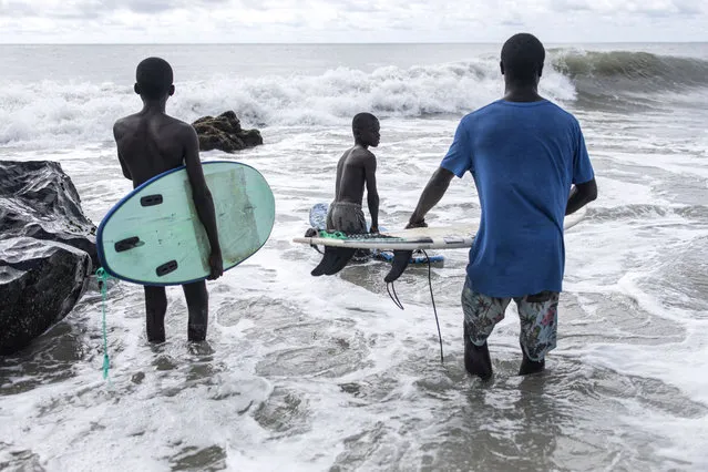 Surfers enter the water in Robertsport on October 5, 2023. Surfing in the fishing town of Robertsport has taken off in the last years, attracting a few tourists and Liberian youth alike. The Robertsport surf club with the aid of an NGO, Provide The Slide, have managed to provide youth with surfboards and in some cases help send the children to school. Senior surfers provide courses for Robertsport youth, teaching them about the ocean, how to swim and how to surf. (Photo by John Wessels/AFP Photo)