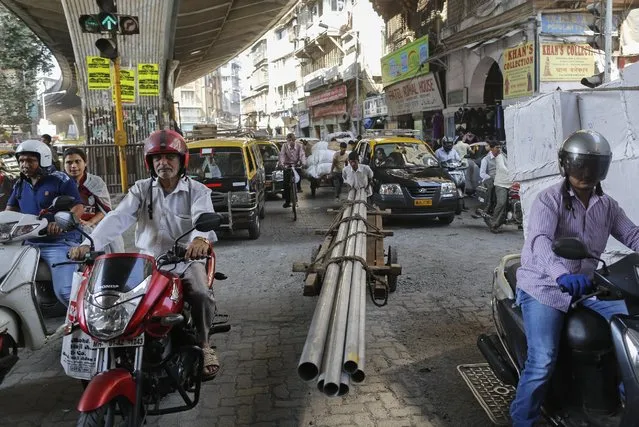 A porter transports metal pipes on a wooden handcart as people wait to cross a street in Mumbai, India, February 8, 2016. (Photo by Danish Siddiqui/Reuters)