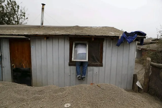 A man uses a window to enter his house at Ensenada town which is covered with ashes from Calbuco volcano near Puerto Varas city, April 23, 2015. (Photo by Ivan Alvarado/Reuters)