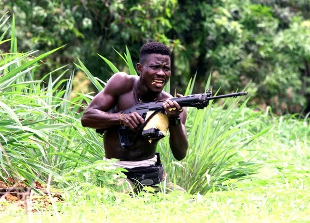 A pro-government Sierra Leonean fighter bites a bullet as he takes position in no man's land 2 km ahead of Rogberi junction where evidence of executed UN troops were found after heavy fighting between government troops and RUF rebels 100 km north east of Freetown, Sierra Leone, May 23, 2000. (Photo by Yannis Behrakis/Reuters)