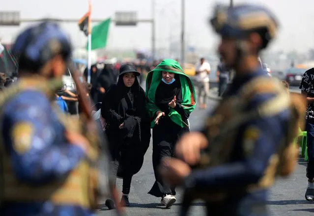 Members of Iraqi security forces stand guard as Shiite pilgrims march from the capital Baghdad to the shrine of Imam Hussein in the central holy city of Karbala, ahead of the Arbaeen religious festival, on September 23, 2021. Each year, Shia pilgrims converge in large numbers to the holy Iraqi cities of Najaf and Karbala ahead of Arbaeen, which marks the 40th day after Ashura, commemorating the seventh century killing of Prophet Mohammed's grandson Imam Hussein. (Photo by Ahmad Al-Rubaye/AFP Photo)