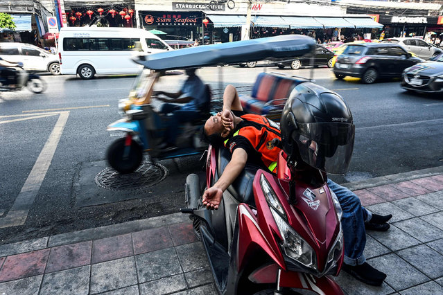 A motorcycle-taxi driver takes a nap while leaning on his bike along a street in Bangkok, Thailand on February 17, 2019. (Photo by Jewel Samad/AFP Photo)