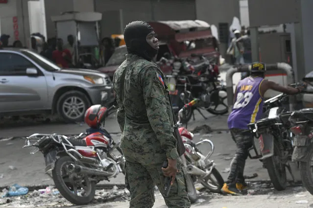 An armed police officer stands outside a gas station after police shot bullets into the air to disperse a crowd threatening to burn down the gas station because the crowd believed the station was withholding gas, in Port-au-Prince, Haiti, Saturday, October 23, 2021. (Photo by Matias Delacroix/AP Photo)