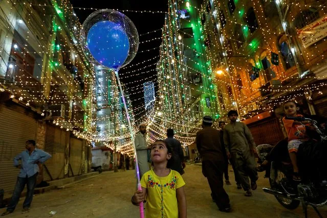 A girl with balloons walks on the eve of Eid-e-Milad-ul-Nabi, the birth anniversary of Prophet Mohammad, in Karachi, Pakistan, October 18, 2021. (Photo by Akhtar Soomro/Reuters)