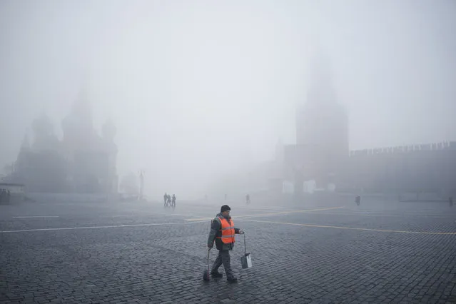 A municipal worker walks in Red square, with the Spasskaya Tower, right, and St. Basil's Cathedral visible through the fog in Moscow, Russia, Tuesday, November 2, 2021. A dense fog engulfed the Russian capital on Tuesday, causing numerous flight delays at Moscow’s airports. (Photo by Pavel Golovkin/AP Photo)
