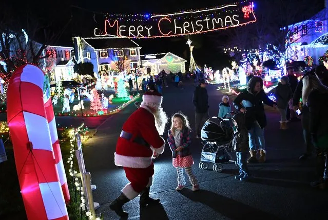 Charlotte Basham, 5, greets Santa Claus along Marshall Pond Road on Sunday December 19, 2021 in Burke, VA. The street has become a destination spot with nearly every house decked out for the season. (Photo by Matt McClain/The Washington Post)
