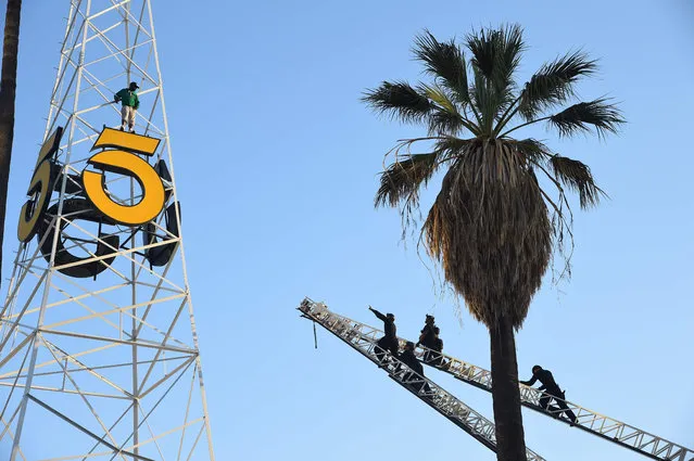 Los Angeles police officers (R) climb two fire ladders to reach a man on the historic KTLA radio tower in Hollywood, California, May 11, 2016. For nearly three hours the man clutched the trestles of the 160-foot (53 meters) tower located at the Sunset Bronson Studios before being safely returned to the ground, where he was taken into police custody for mental evaluation. (Photo by Robyn Beck/AFP Photo)
