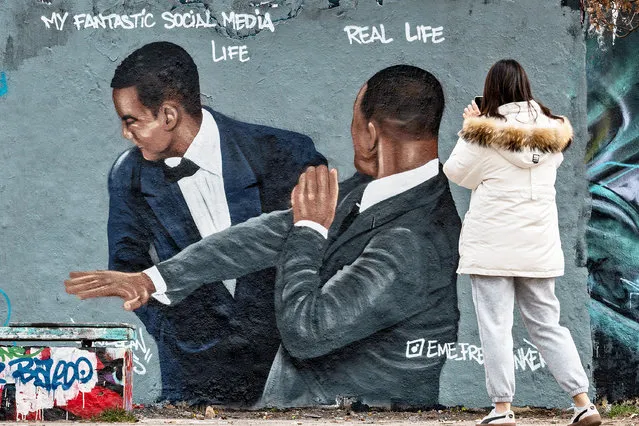 A woman takes a photo of a mural by Berlin-based street artist Eme Freethinker featuring the likeness of US actor Will Smith (R) slapping US comedian Chris Rock during the Oscars ceremony, in Berlin on March 30, 2022. (Photo by John MacDougall/AFP Photo)