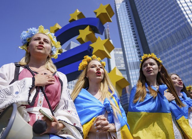 Women with flower decorations around their heads sing the Ukrainian national anthem below the Euro Monument during a demonstration under the slogan “Mothers against the war in Ukraine and Europe”, in Frankfurt, Germany, Sunday, May 8, 2022. (Photo by Frank Rumpenhorst/dpa via AP Photo)