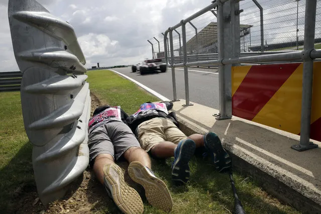 Photographers lie downy by the side of the track to shoot the cars passing by during the first free practice at the Silverstone racetrack, in Silverstone, England, Friday, July 12, 2019. The British Formula One Grand Prix will be held on Sunday. (Photo by Luca Bruno/AP Photo)