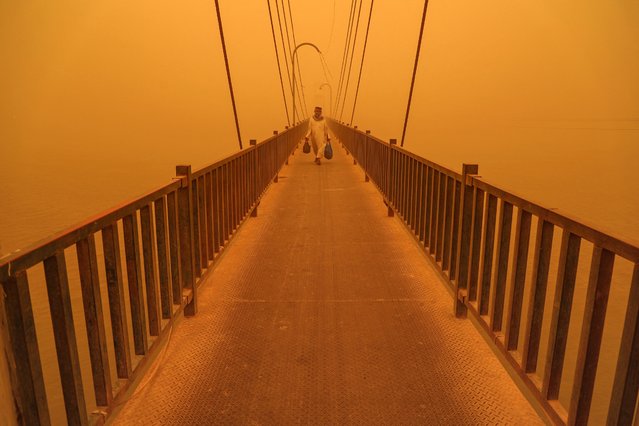 A man walks along a pedestrian bridge along the Euphrates river in the city of Nasiriyah in Iraq's southern Dhi Qar province on May 16, 2022 amidst a heavy dust storm. (Photo by Asaad Niazi/AFP Photo)