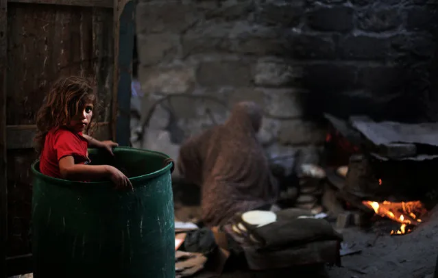 In this Monday, June 20, 2016 photo, a Palestinian girl plays in a barrel as her mother bakes bread for a Ramadan dinner at their house in el-Zohor slum, on the outskirts of Khan Younis refugee camp, southern Gaza Strip. (Photo by Khalil Hamra/AP Photo)