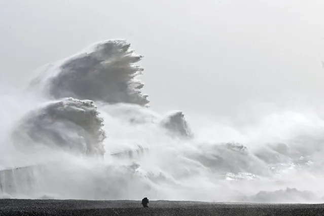 A photographer kneels on the beach as waves crash over Newhaven harbour wall in Newhaven, southern England on February 18, 2022, as Storm Eunice brings high winds across the country. Britain put the army on standby Friday and schools closed as forecasters issued two rare “red weather” warnings of “danger to life” from fearsome winds and flooding due to the approaching storm Eunice. (Photo by Glyn Kirk/AFP Photo)