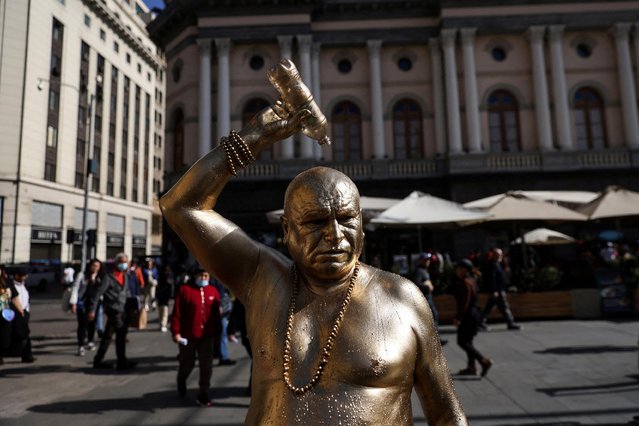 A human living statue portraying Buddha holds a bottle as he takes a break during an unusual winter period heatwave in Santiago, Chile on August 4, 2023. (Photo by Ivan Alvarado/Reuters)