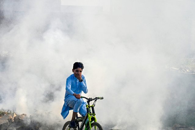 A boy rides past as smoke billows from a burning garbage dump, in Lahore on November 1, 2024. (Photo by Arif Ali/AFP Photo)