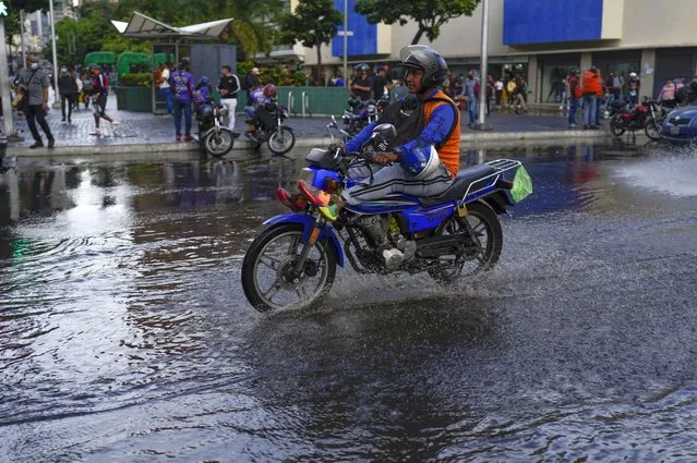 A man rides his motorcycle over a puddle in Caracas, Venezuela, Wednesday, June 29, 2022. (Photo by Ariana Cubillos/AP Photo)