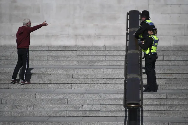 Police officers talk to a man keeping the two meter social distance, in a deserted Trafalgar Square, due to the Coronavirus outbreak, in London, Tuesday, April 14, 2020. (Photo by Alberto Pezzali/AP Photo)