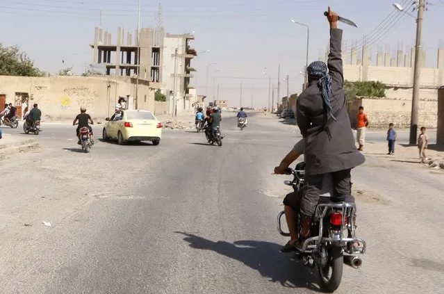 A man holds up a knife as he rides on the back of a motorcycle touring the streets of Tabqa city with others in celebration after Islamic State militants took over Tabqa air base, in nearby Raqqa city August 24, 2014. (Photo by Reuters/Stringer)