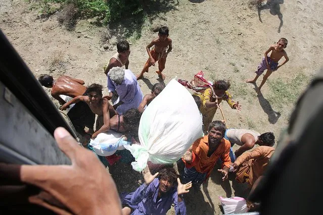 Flood-affected people scuffle for food bags distributed from a helicopter by Pakistan army in Dadu district of Sindh province on September 1, 2022. Army helicopters flew sorties over cut-off areas in Pakistan's mountainous north on August 31 and rescue parties fanned out across waterlogged plains in the south as misery mounted for millions trapped by the worst floods in the country's history. (Photo by Husnain Ali/AFP Photo)