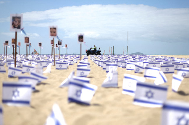 A policeman passes by, as Israel flags and pictures symbolising victims are placed in Copacabana beach by NGO Rio de Paz, one month on from the October 7th attack by the Palestinian Islamist group Hamas, in Rio de Janeiro, Brazil on November 7, 2023. (Photo by Ricardo Moraes/Reuters)